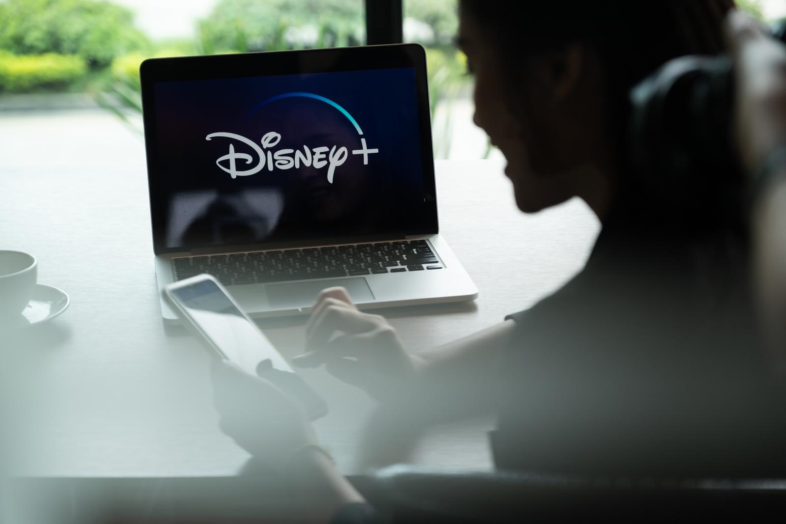 In 2024, a woman is buying Disney+ at a cheap price using her laptop, which prominently displays the Disney Plus logo.