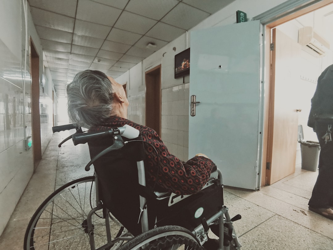 An elderly woman in a wheelchair looking out the door of a hospital.