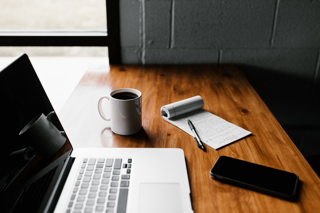 A laptop sits on a wooden table next to a cup of coffee.