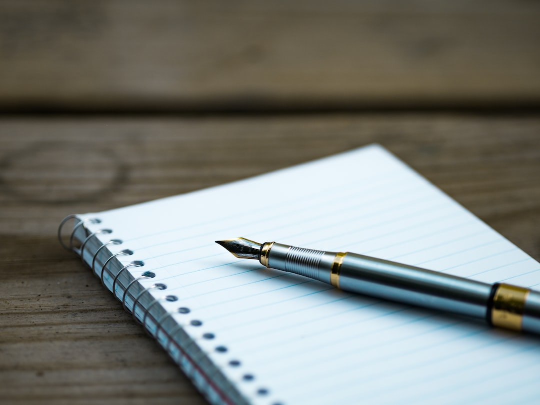 A pen sits on top of a notebook on a wooden table.