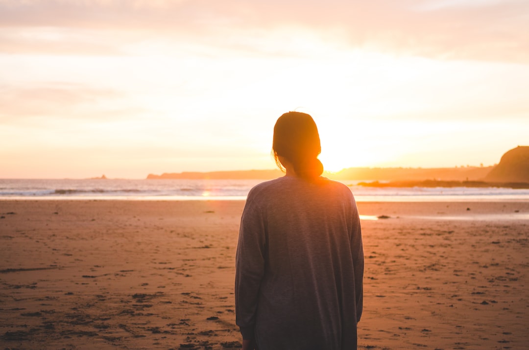 A woman standing on the beach at sunset.