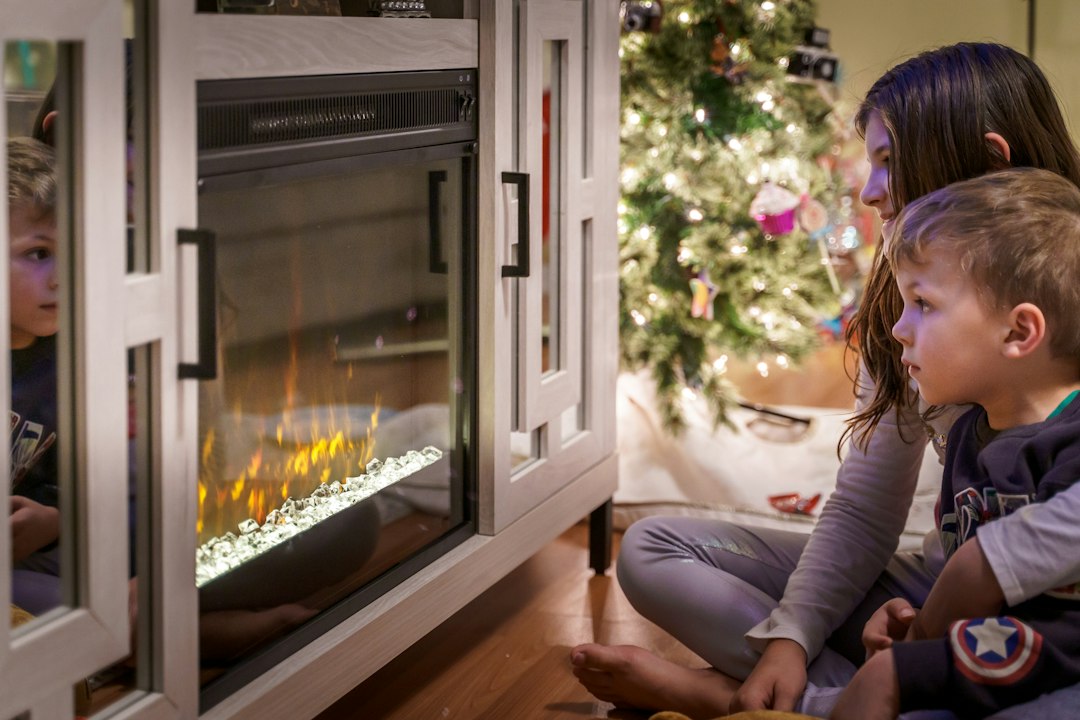 Two children looking at a christmas tree in front of a fireplace.