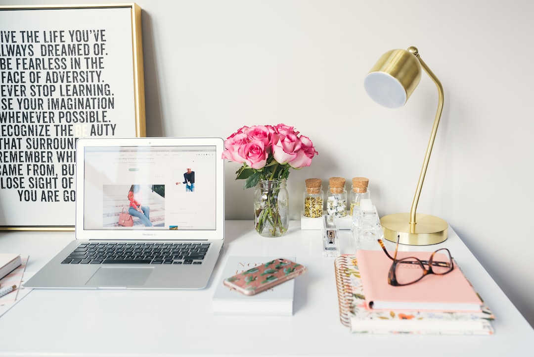 A desk with a laptop, books, flowers and a poster.