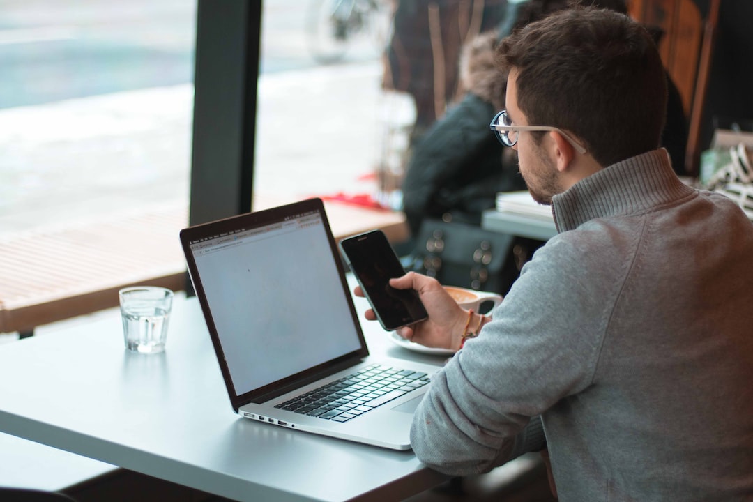 A man sitting at a table with a laptop and cell phone.