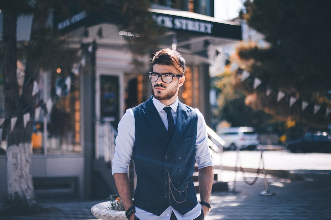 A man wearing glasses and a vest standing on a street.